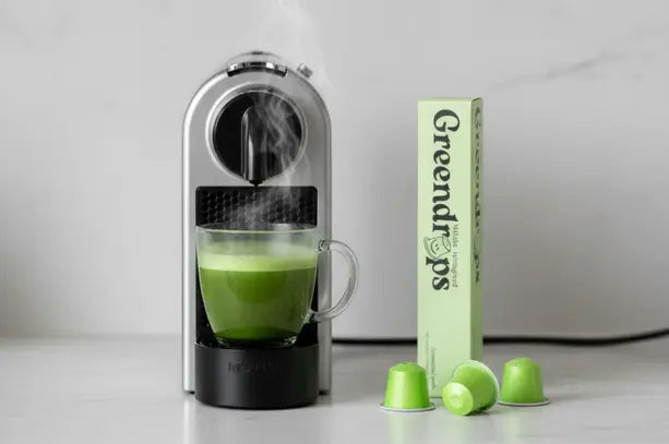Matcha Capsules verpakking naast een Nespresso toestel met doorschijnende kop matcha thee